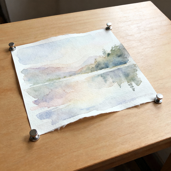 Artwork placed face-up on a flat table with small weights holding the corners flat